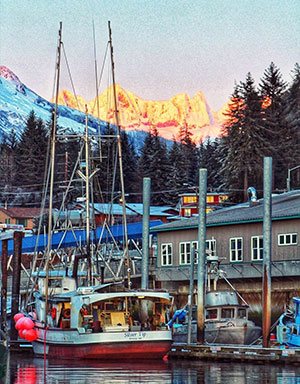 Photo of a docked fishing vessel with city and mountains in the background