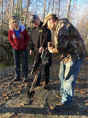 Man demonstrating crossbow to two other people