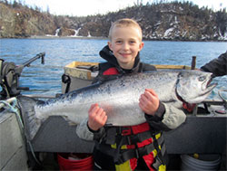 A boy holding a large Chinook salmon.