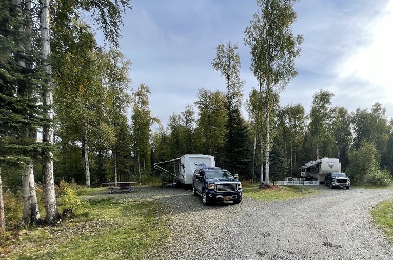 Truck pulling a RV at a campground surrounded by trees