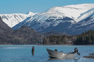 An angler fishes the Kenai River with scenic snow-covered mountains in the background
